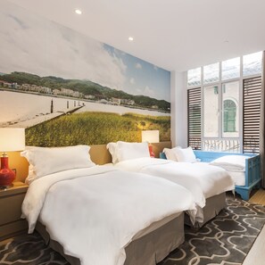 Quarto de hotel com duas camas, uma janela grande com persianas, um mural de paisagem e um tapete estampado.