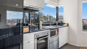 A modern kitchen with a large window, built-in oven, and stainless steel appliances. - 110 Hampden Apartments (Battery Point)