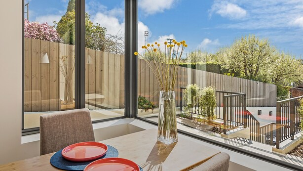 A modern dining area with a large window, a wooden fence, and a view of the garden. - 110 Hampden Apartments (Battery Point)