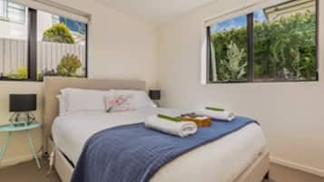 A bedroom with a bed, a bedside table, a window with a view of greenery, and a wall-mounted TV.