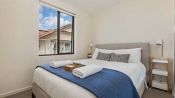 A hotel room with a bed, a window, a bedside table, and a lamp.