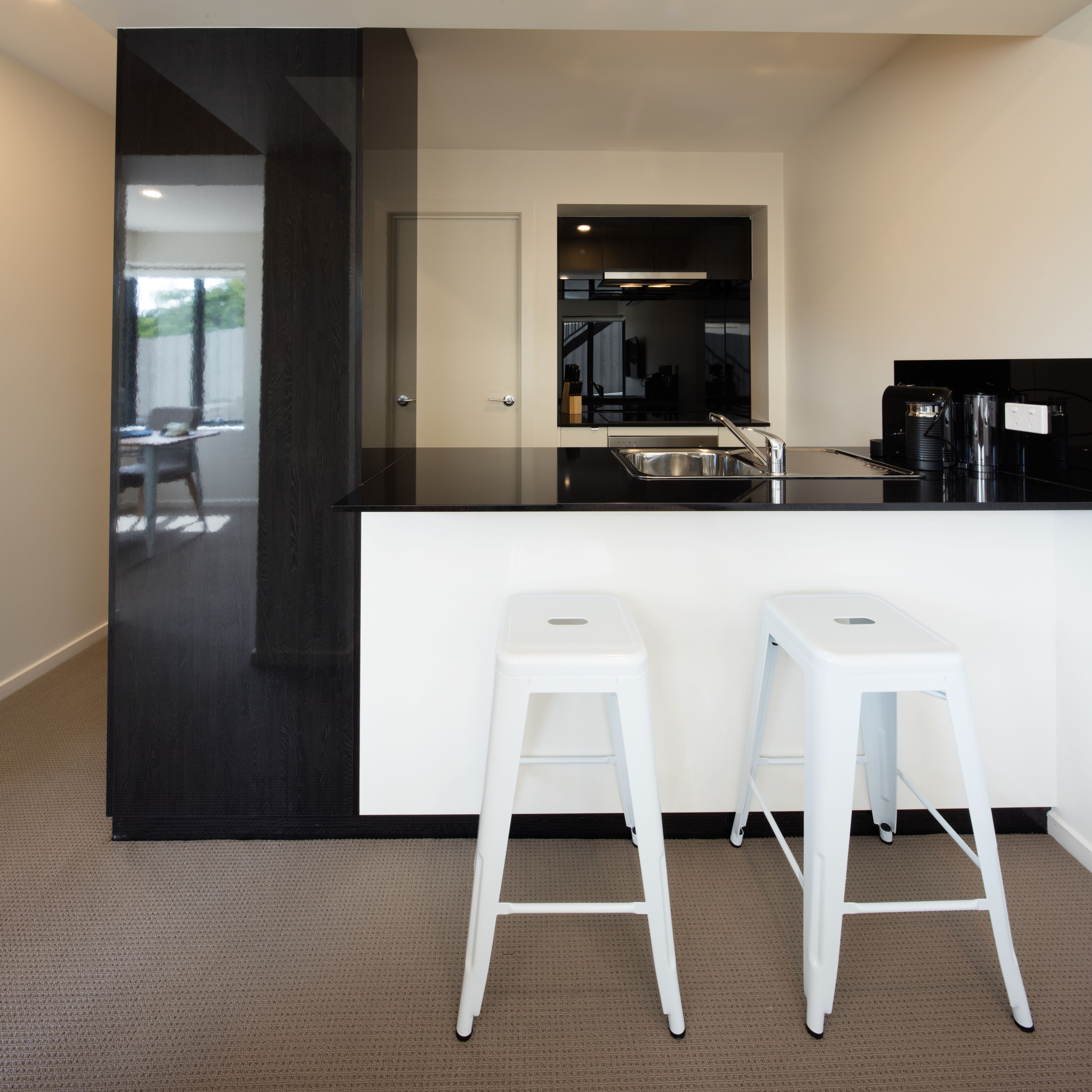 A modern kitchen with a black countertop, white stools, and a large mirror above the sink.