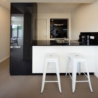 A modern kitchen with a black countertop, white stools, and a large mirror above the sink.