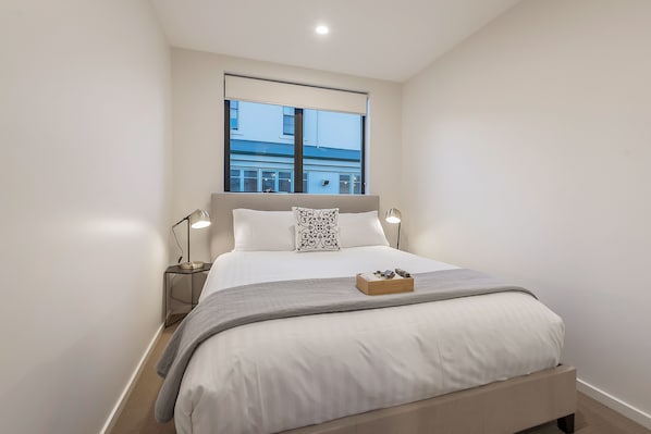 A modern bedroom with a large bed, bedside lamps, a window, and a view of the outside.