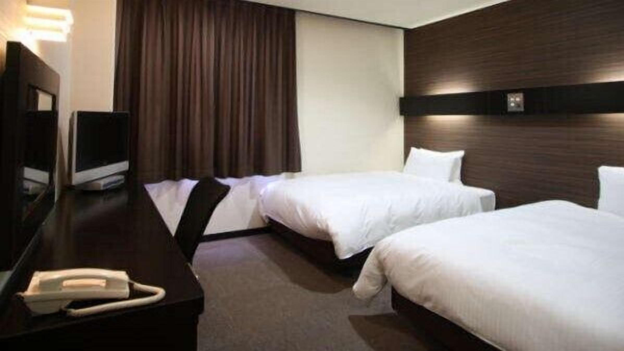 A hotel room with two beds, a desk with a telephone, and a TV.