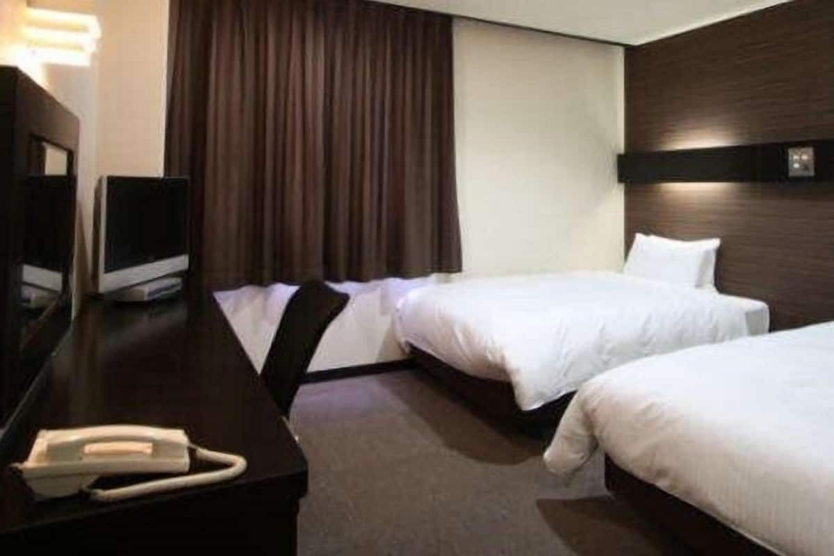 Ein Hotelzimmer mit zwei Betten, einem Schreibtisch mit Telefon und einem Fernseher.