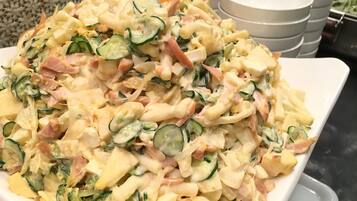 A large white plate filled with a creamy pasta salad, containing ingredients like zucchini, ham, and cheese.