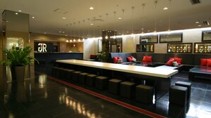 Eine moderne Bar mit einer langen Theke, mehreren Barhocker und einer Sitzecke mit roten Kissen.