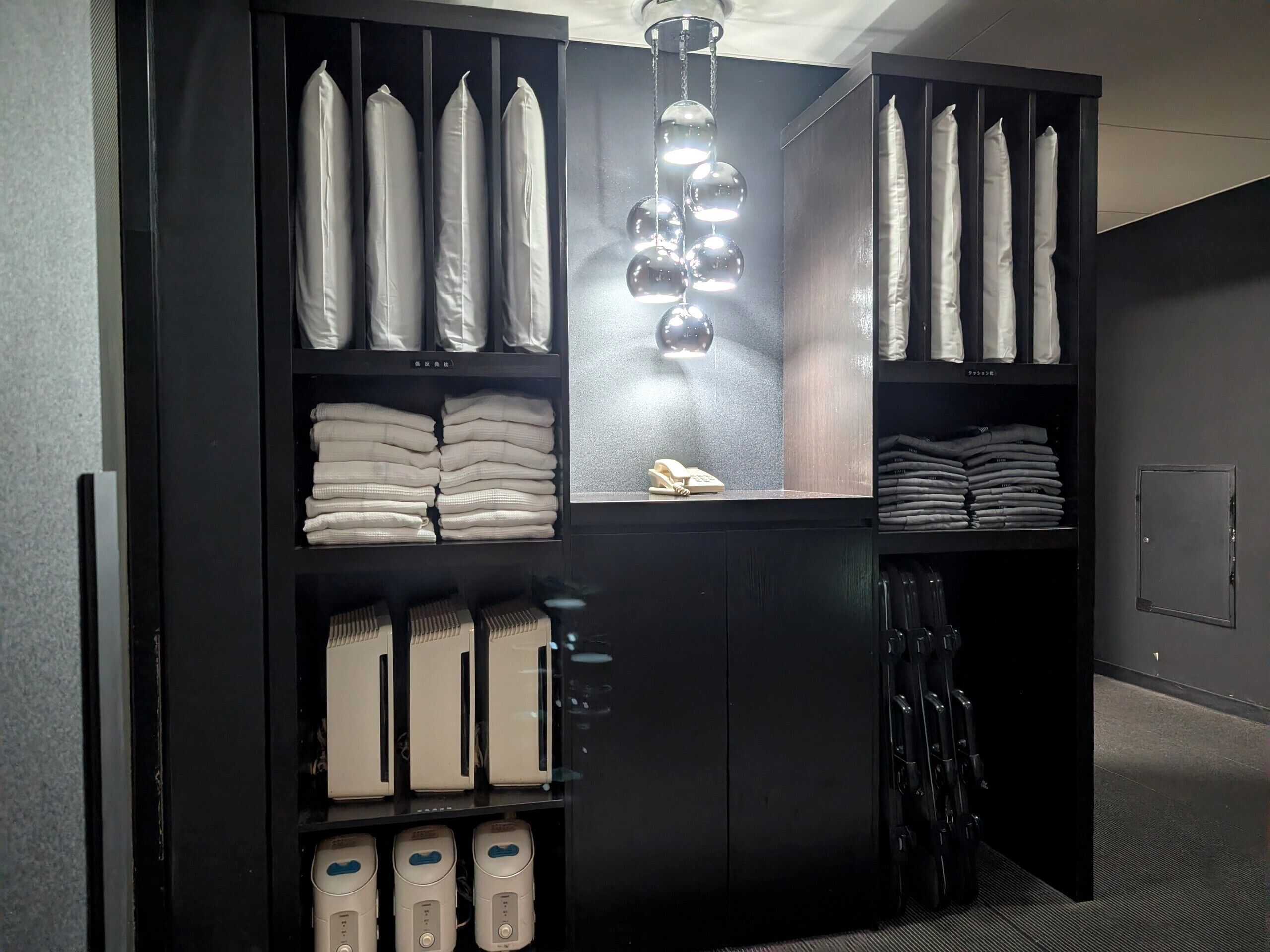A storage unit with neatly folded towels, a phone, and a heater.