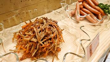 Eine Auswahl an Speisen, darunter eine Portion gehobelte Gemüse mit Sesam, eine Schüssel Würstchen und eine kleine Schüssel Salat.