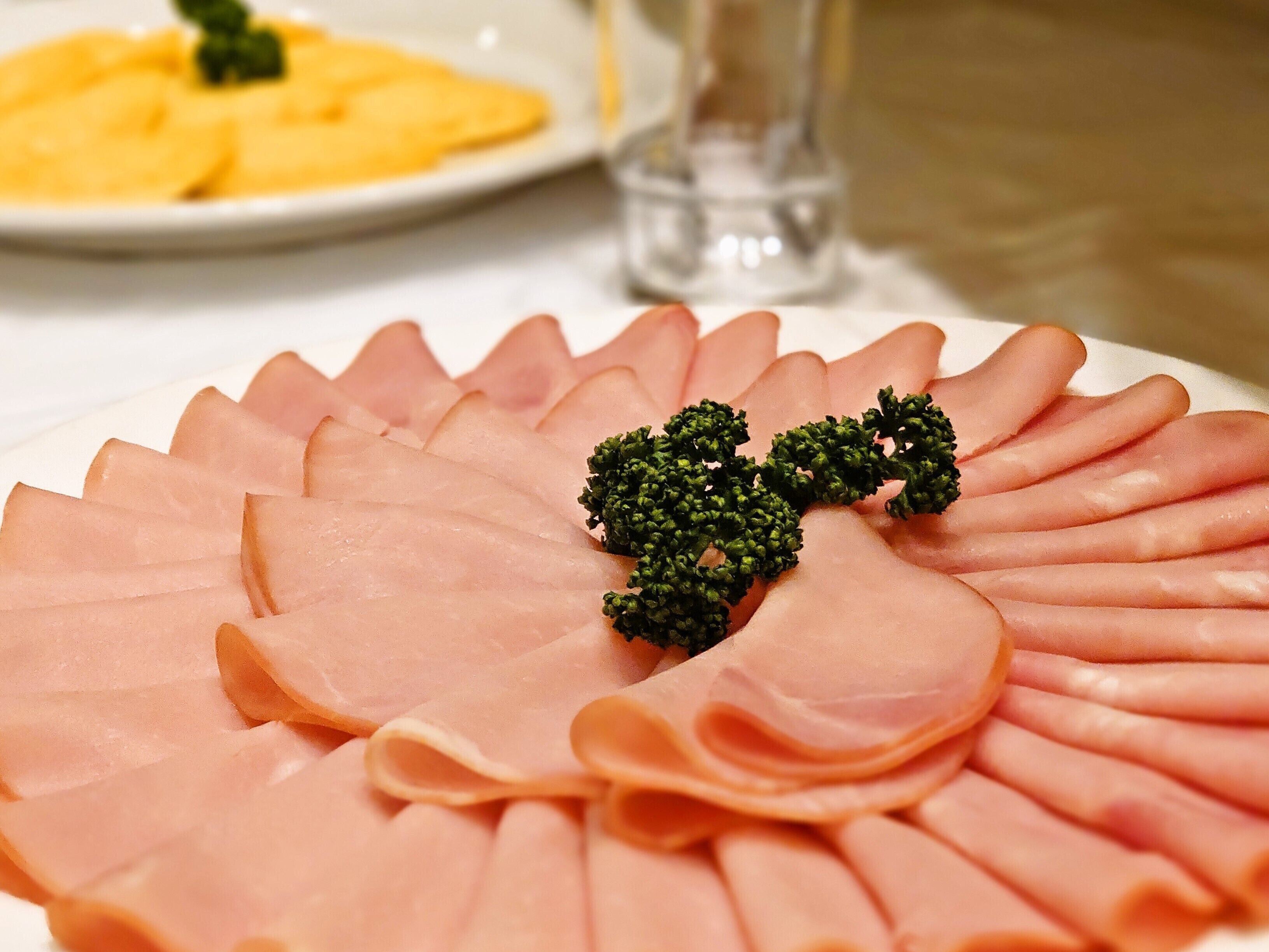 A plate of neatly arranged sliced ham with a decorative broccoli garnish.