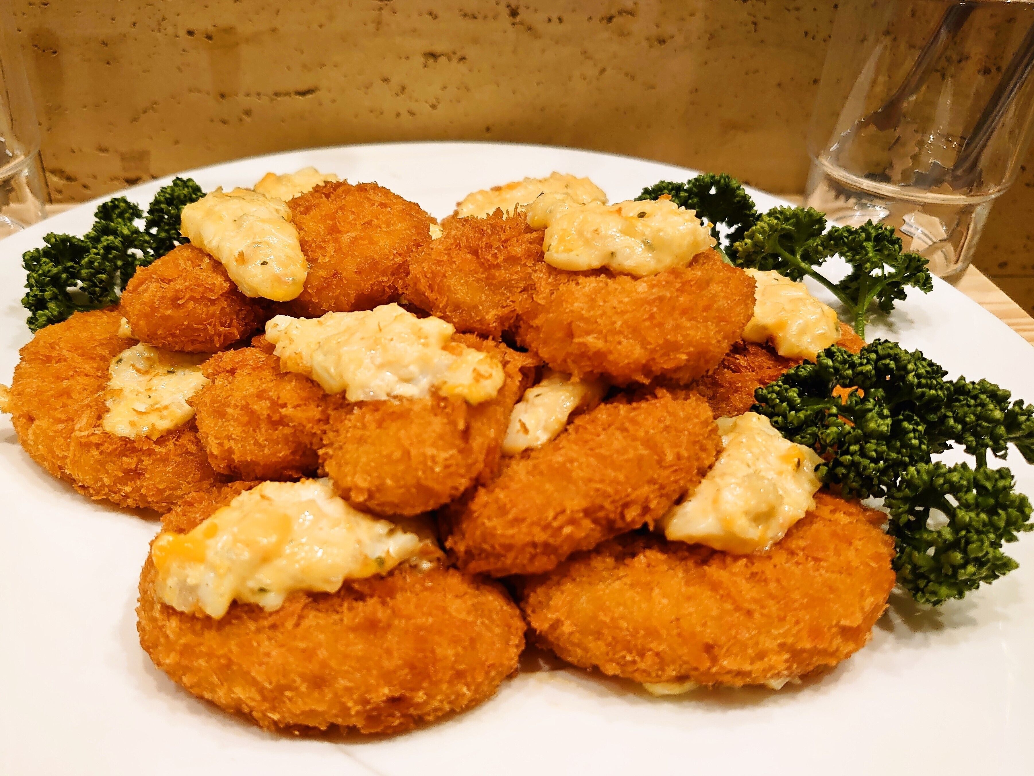 Ein Teller mit paniertem und frittiertem Essen, möglicherweise Chicken Nuggets, mit cremiger Soße und Brokkolidekor.