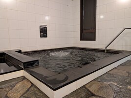 Un jacuzzi con pared de azulejos y un cartel con texto en japonés.
