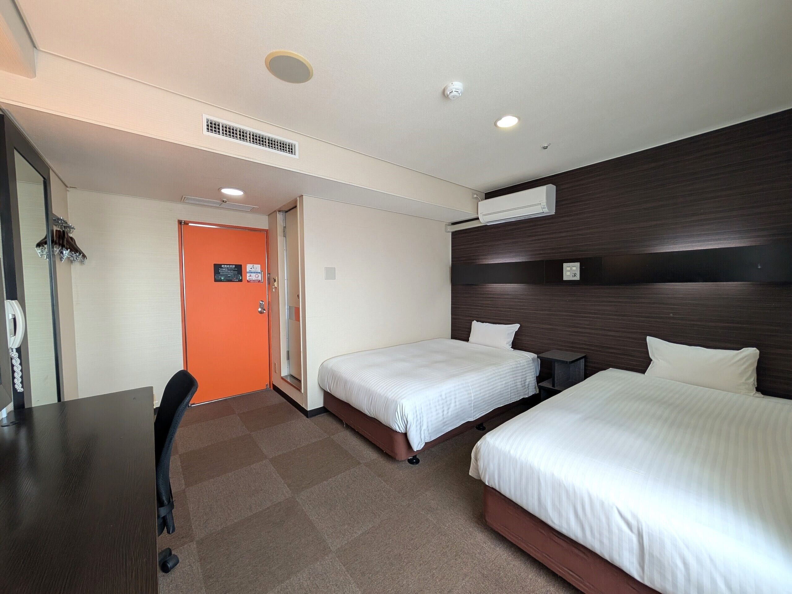 Ein Hotelzimmer mit zwei Betten, einem Schreibtisch und einer Badezimmertür.