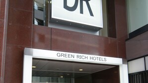 Der Eingang zu Green Rich Hotels mit einer Glastür und einem schwarzen Teppich mit 'DR'-Beschriftung.