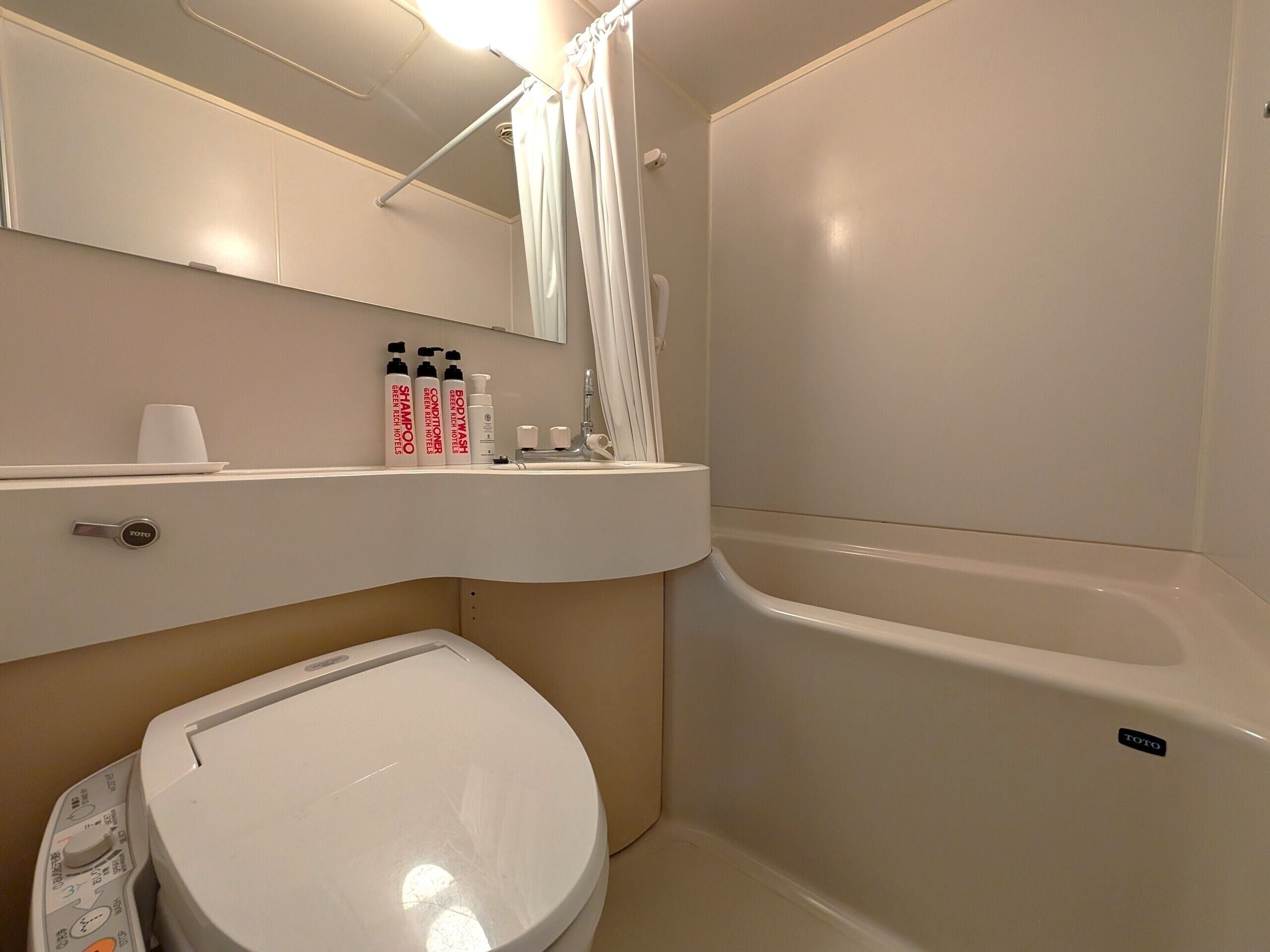 A bathroom with a toilet, a sink, a shower, and a mirror.