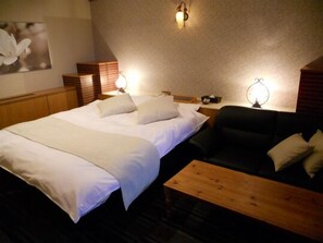 A hotel room with a large bed, two bedside tables, a wooden coffee table, a black armchair, and wall-mounted lamps. - Watergate Gifu (Gifu)