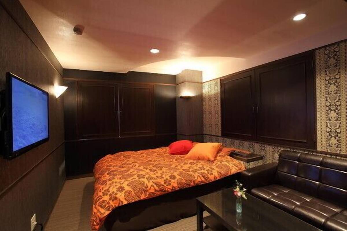 A hotel room with a large bed, a leather sofa, a flat-screen TV, and built-in cabinets.