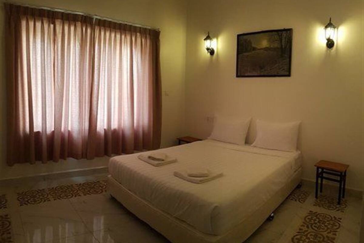 Una habitación de hotel con una cama grande, dos mesitas de noche, un buró, un cuadro en la pared y una ventana con cortinas.