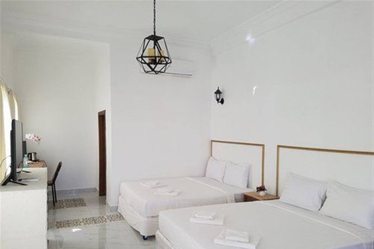 Habitación de hotel con dos camas, un escritorio con computadora y una lámpara colgante.