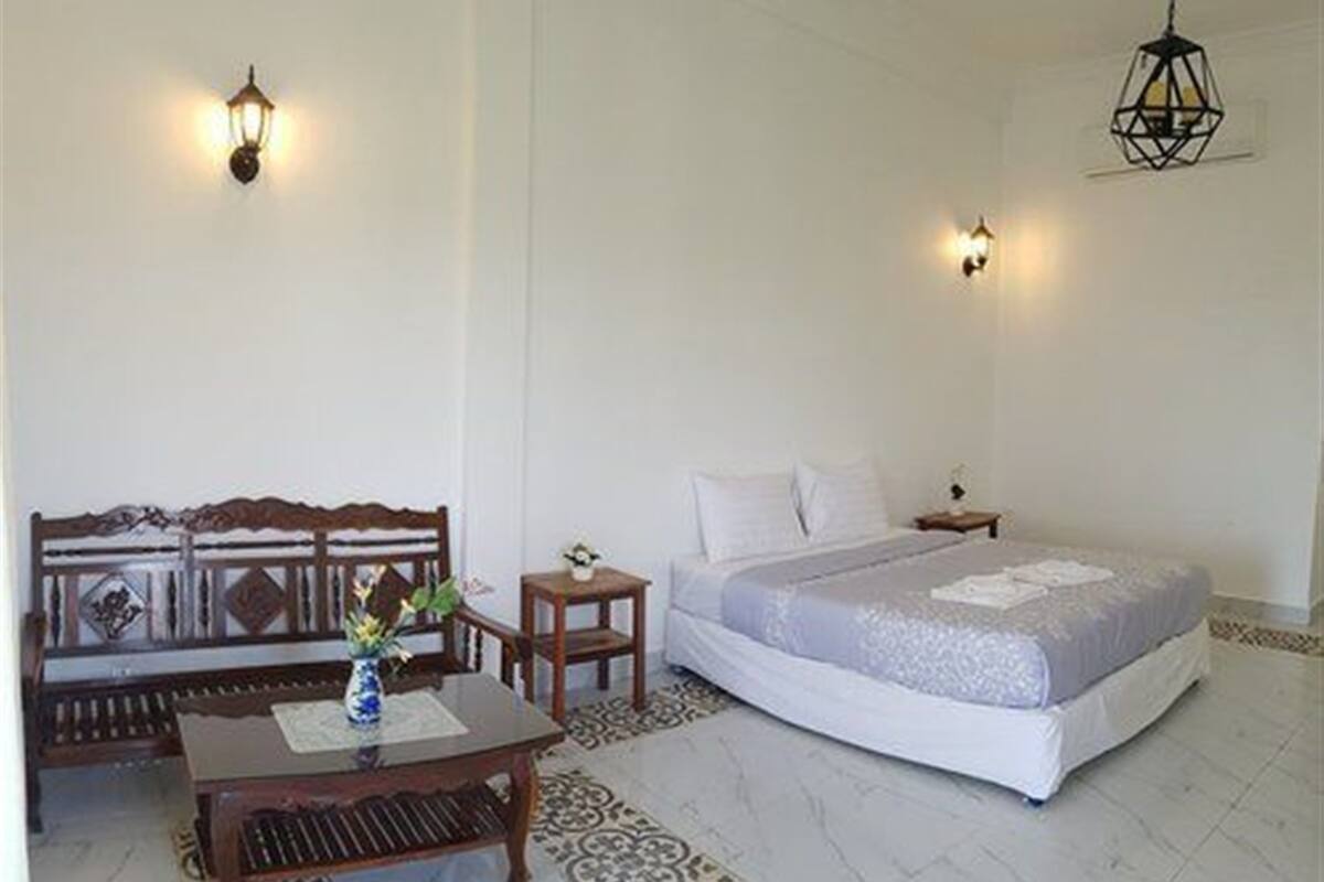 Un dormitorio con una cama, un banco de madera, una mesita con un florero y dos luces fijadas a la pared.