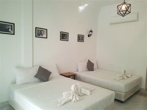 A hotel room with two beds, a small table, and a wall-mounted air conditioner.