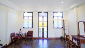 A room with two windows, a table with chairs, and a wooden chair with a cushion. - Baba La Casa Hotel (Chalong)