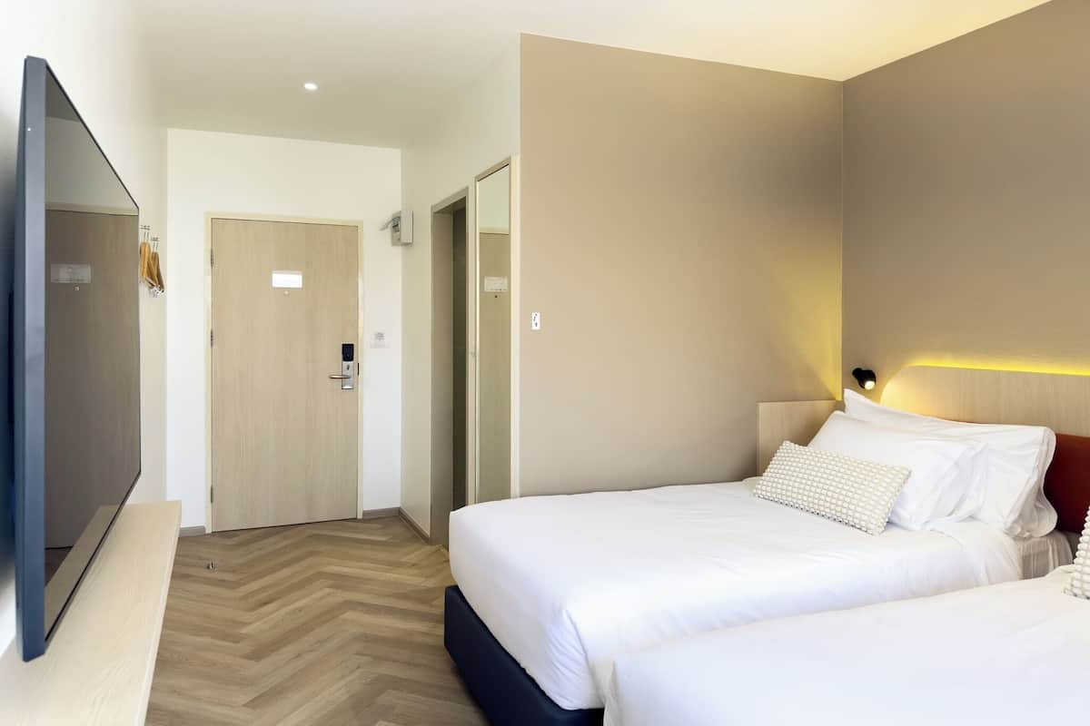 A hotel room with two beds, a flat-screen TV, a wooden floor, and a modern design.