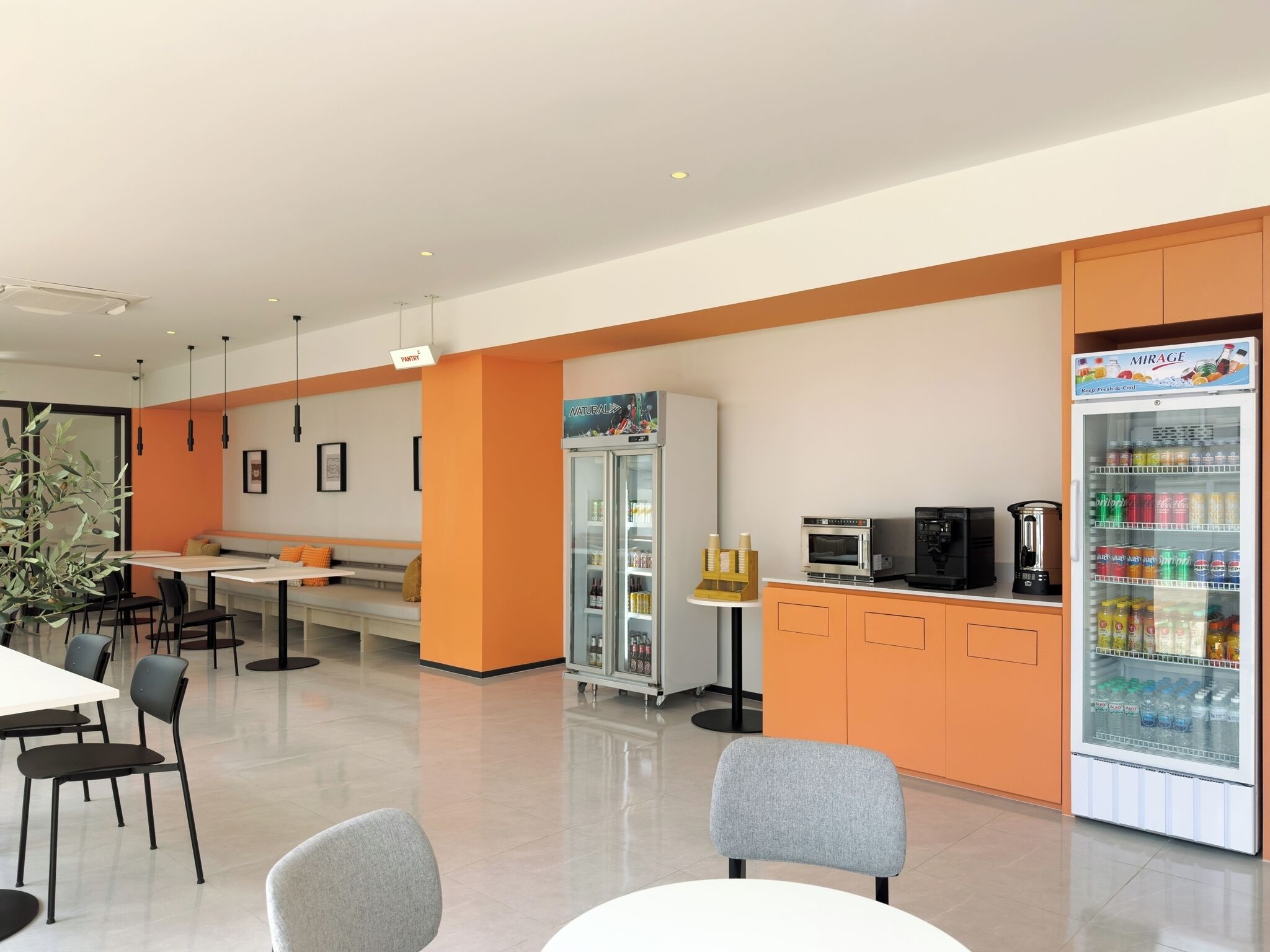 A modern cafe with a seating area, a refrigerator stocked with beverages, and a coffee machine.