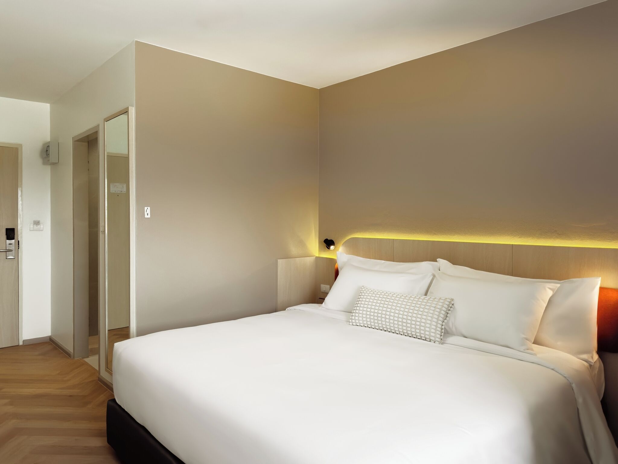 Ein modernes Hotelzimmer mit einem großen Bett, Holzboden und einer neutralen Farbgestaltung.