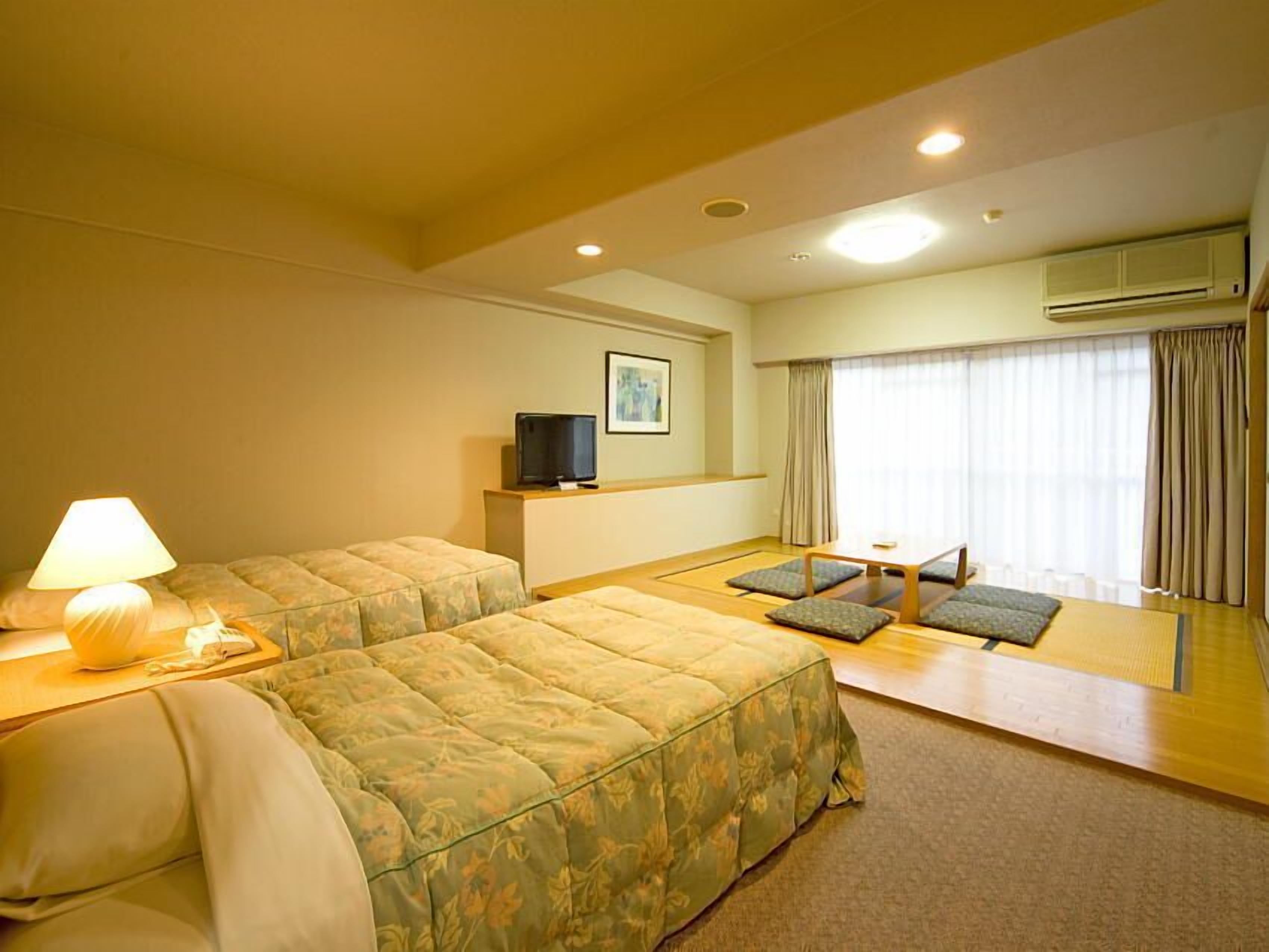 A hotel room with two beds, a TV, a lamp, a window with curtains, and an air conditioning unit.