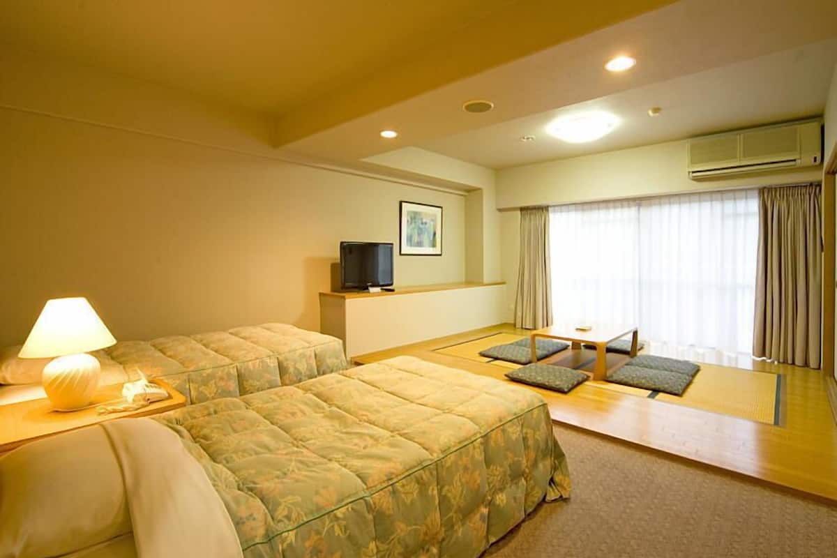 A hotel room with two beds, a TV, a lamp, a window with curtains, and an air conditioning unit.