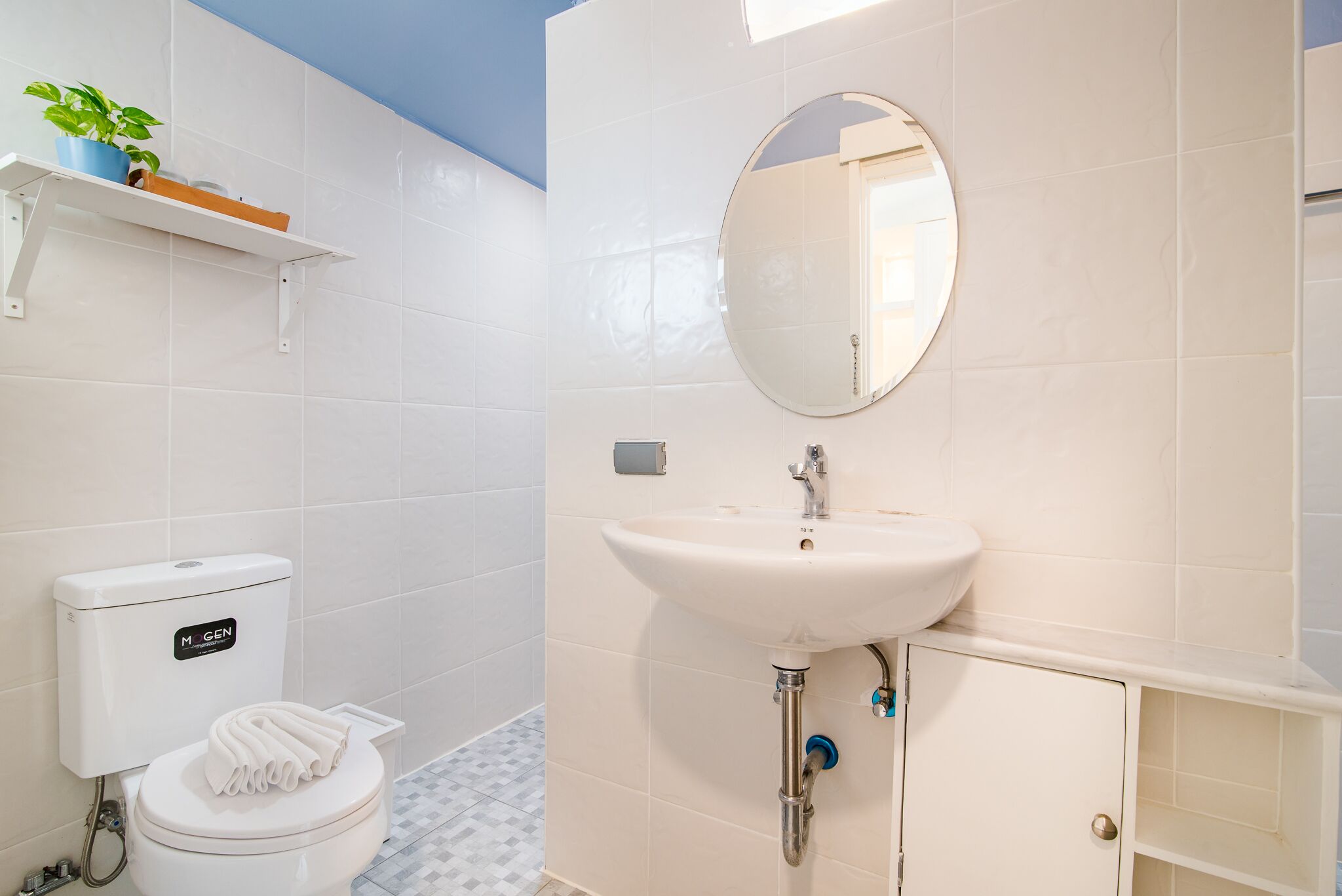 Une salle de bain équipée de toilettes, d’un lavabo, d’un miroir et d’une étagère sur laquelle est posée une plante.