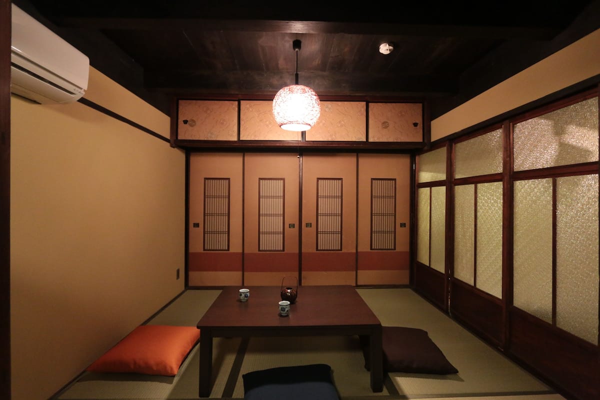 Una habitación tradicional japonesa con suelo de tatami, una mesa baja con cojines y puertas correderas con paneles decorativos.
