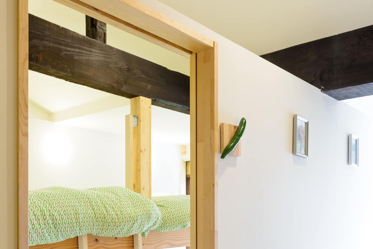 Una cama litera con escalera, un cojín verde estampado y una estructura de vigas de madera.