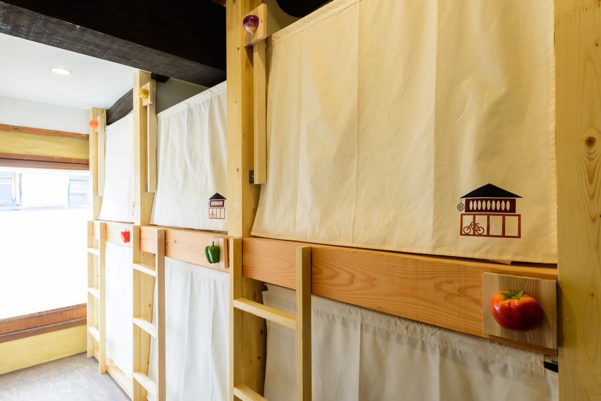 Una habitación con literas de madera, cada una con un pequeño estante y una bolsa colgada.