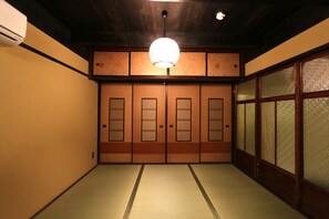 Ein traditioneller japanischer Raum mit Tatami-Boden, Schiebetüren und einer hängenden Leuchte.