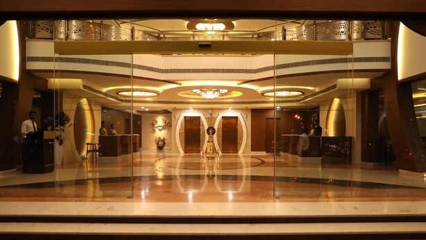 A spacious lobby with a central reception desk, a chandelier, and a glass railing overlooking the lower level. - The Thangam Grand (Madurai)