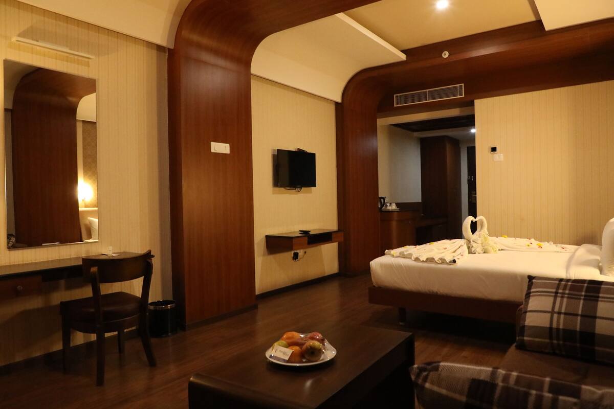 A hotel room with a bed, a desk, a chair, a television, and a fruit bowl.