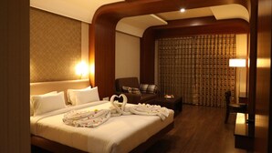 A hotel room with a large bed, a sitting area with a chair and a table, and a curtain-covered window. - The Thangam Grand (Madurai)
