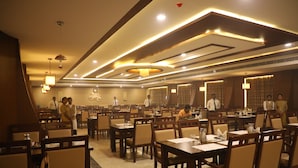 A spacious restaurant with multiple dining tables and chairs, a modern ceiling design, and ambient lighting. - The Thangam Grand (Madurai)