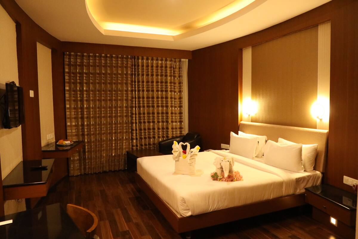 A hotel room with a large bed, a desk, a chair, a TV, and a curtain.