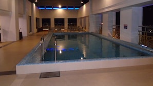 An indoor swimming pool with a tiled edge, surrounded by white walls and a wooden deck. - The Thangam Grand (Madurai)