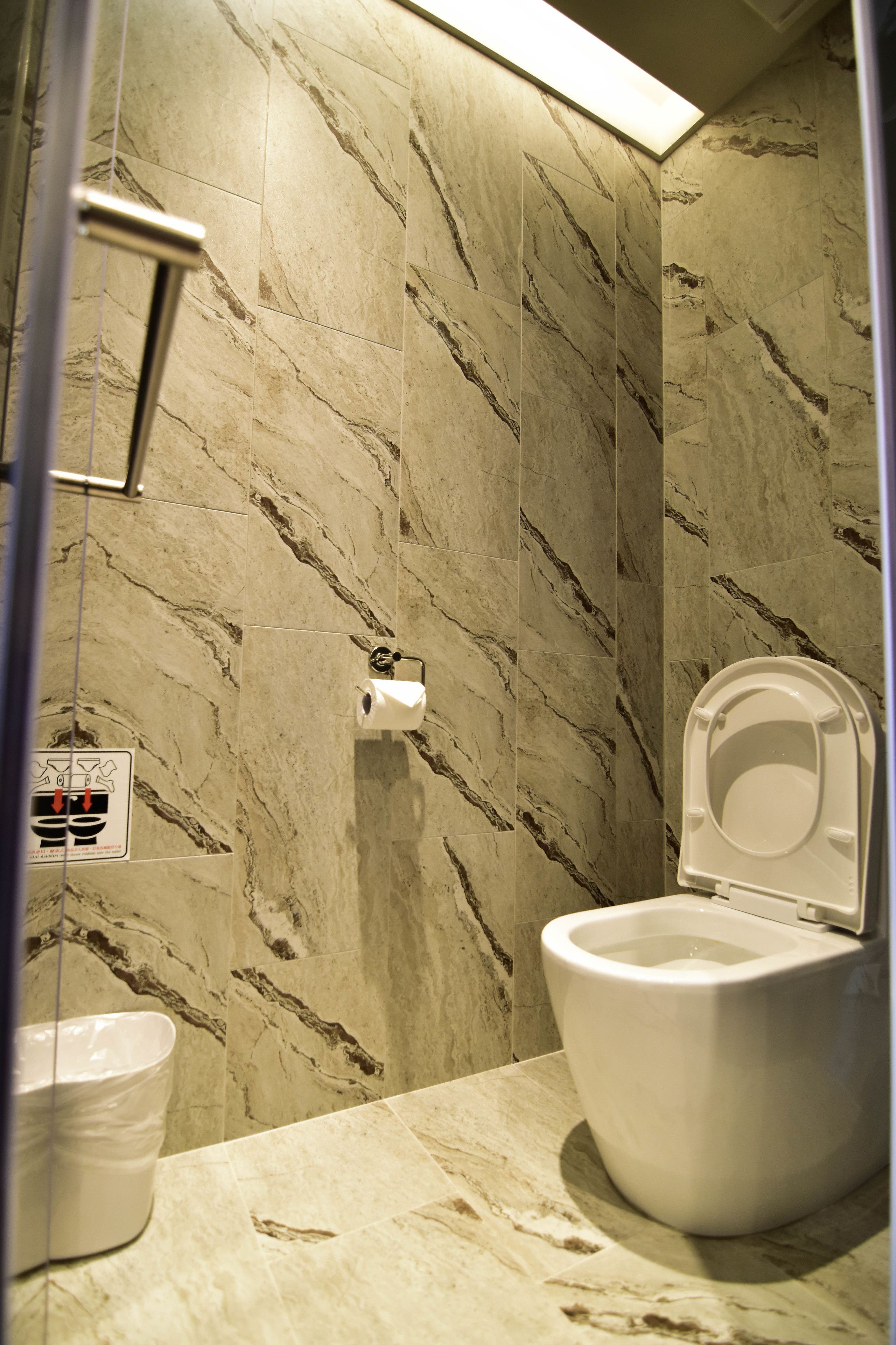 A bathroom with a toilet, marble walls, and a hand dryer.