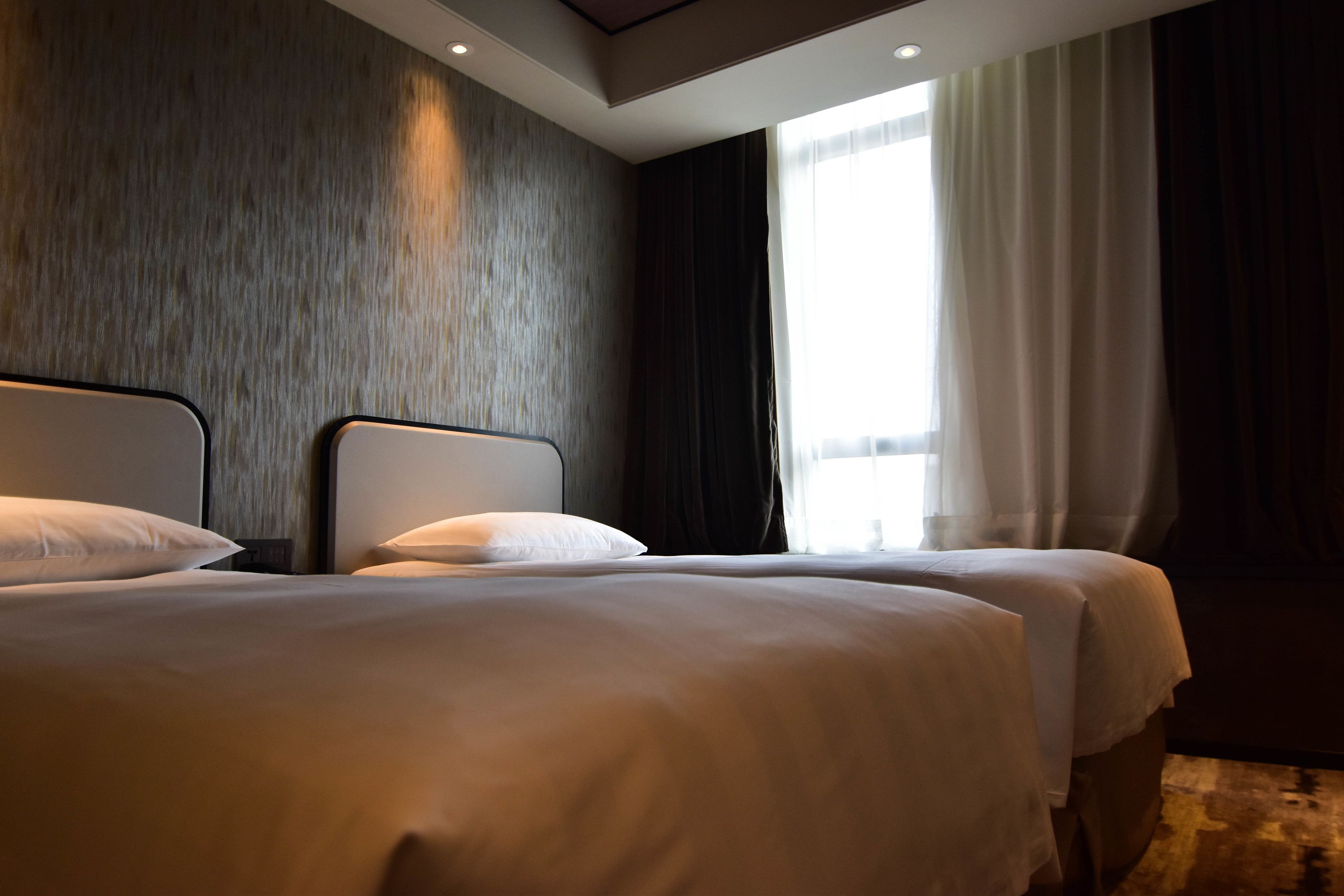 A hotel room with two beds, a large window with curtains, and a modern ceiling design.