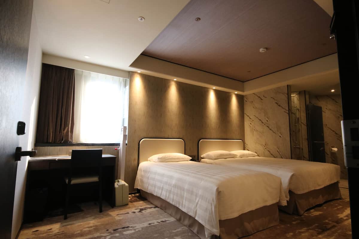A modern hotel room with a desk, two beds, a large mirror, and a marble accent wall.