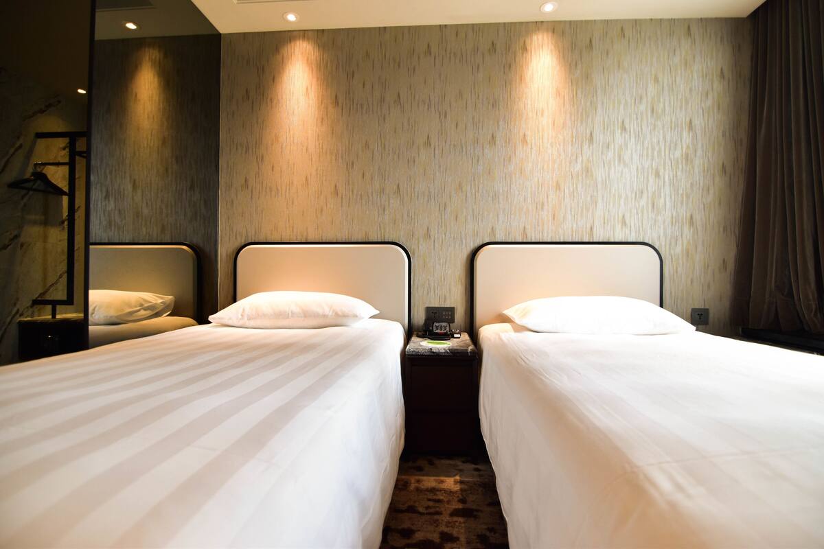 A hotel room with two single beds, a nightstand with a phone, and a mirror on the left wall.