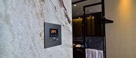 Un baño con un termostato digital que muestra 25°C, una pared de mármol y un perchero con toallas.