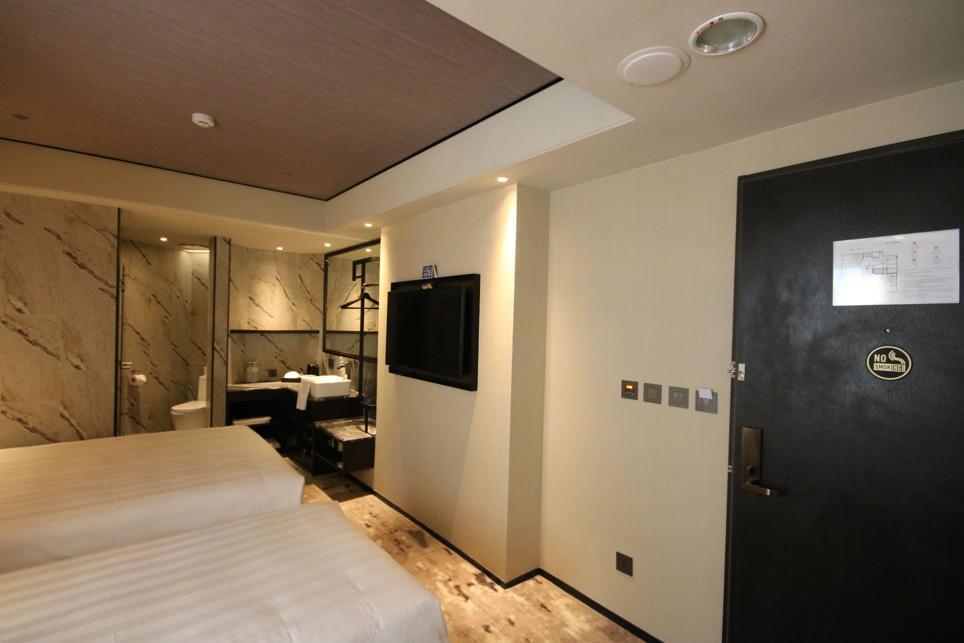 A hotel room with a large bed, a bathroom with a mirror, and a door with a no smoking sign.