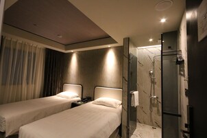 Habitación de hotel con dos camas, zona de ducha y mampara de vidrio.